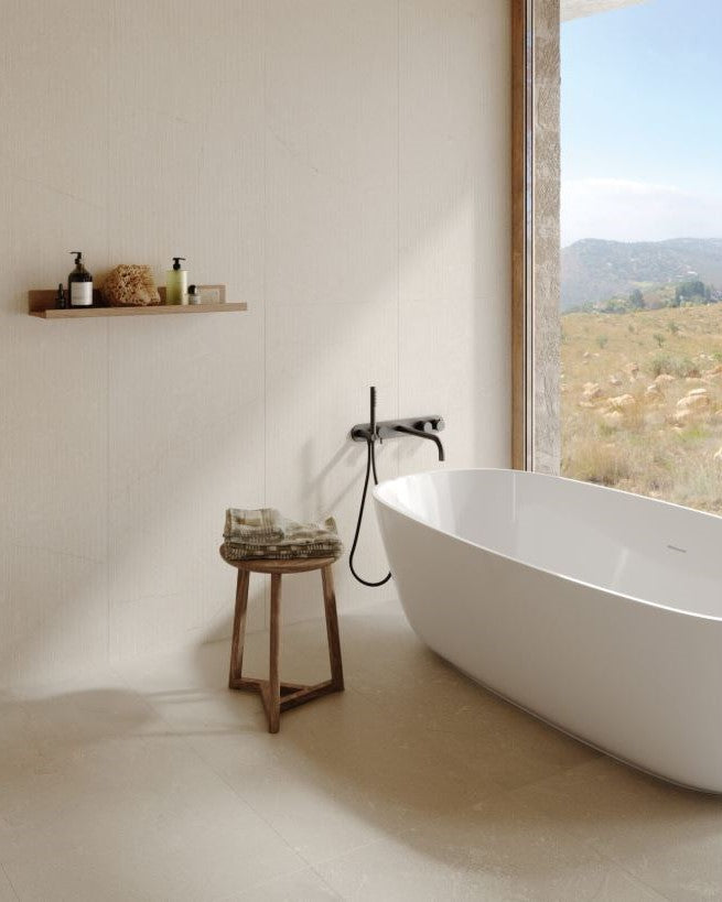 Modern bathroom with a freestanding bathtub, wooden stool, and shelf with toiletries. Modern bathroom and living with 600x600 Pietra Di Sicilia Stone Look Matt Tiles by Marazzi. Melbourne, Geelong, Shepparton, Ballarat, Bendigo, Mornington, Bellarine, Peninsula, Melton, Lara, Sunbury, Warrnambool, Horsham tiles. Victoria and Nationwide Delivery. Australia.